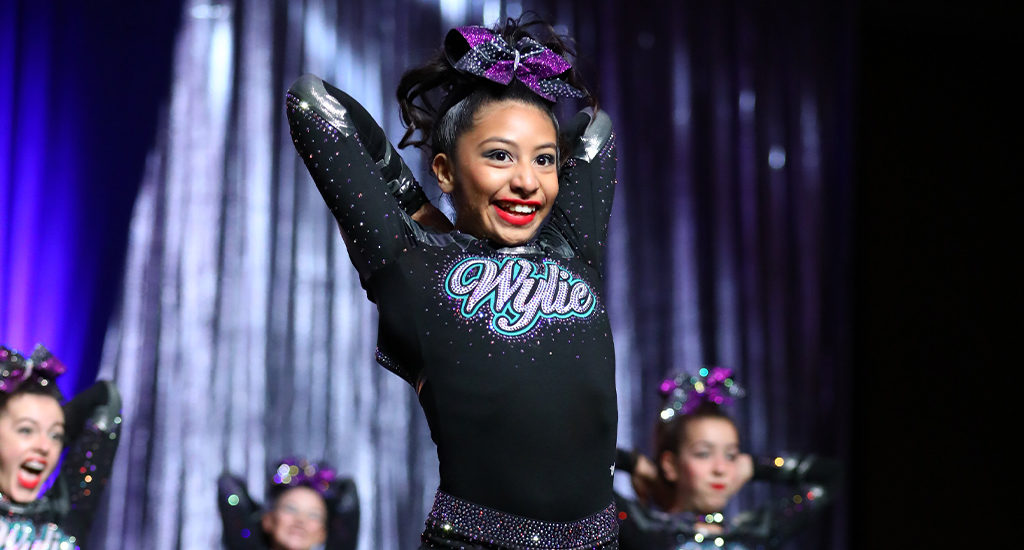 Cheerleader smiles with her arms behind her head in a routine